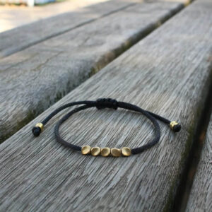 Handmade Eternal Glow Bracelet with black cord and gold beads on wooden background