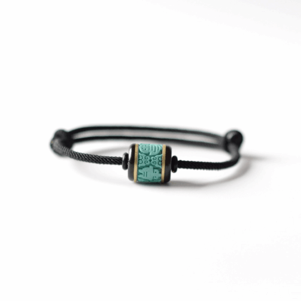 Black cord bracelet with a sliding knot and a carved barrel bead in a faux turquoise style, serving as a Chinese luck charm.